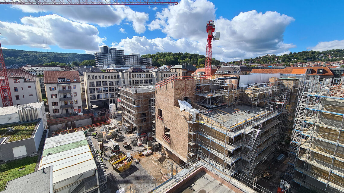 Luftaufnahme der Baustelle auf dem Klett-Areal in Stuttgart mit eingerüsteten Gebäuden, einem roten Baukran, historischen Klinkerfassaden und Blick über die Stadt unter blauem Himmel.